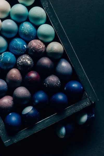 Top view of colored painted easter eggs in wooden box on dark table — Stock Photo