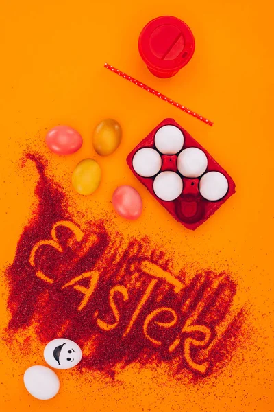 Vista superior del letrero de Pascua hecho de arena roja con huevos de pollo y café en naranja - foto de stock