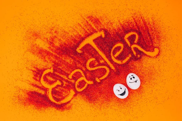 Top view of easter sign made of red sand with chicken eggs with smileys on orange — Stock Photo