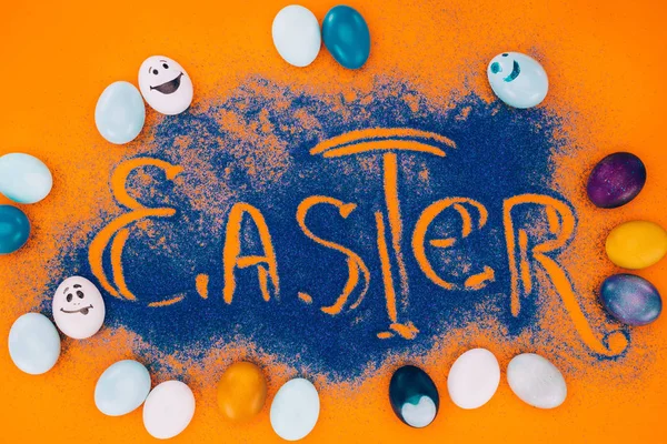 Vista dall'alto del cartello pasquale in sabbia blu con uova dipinte su arancione — Foto stock