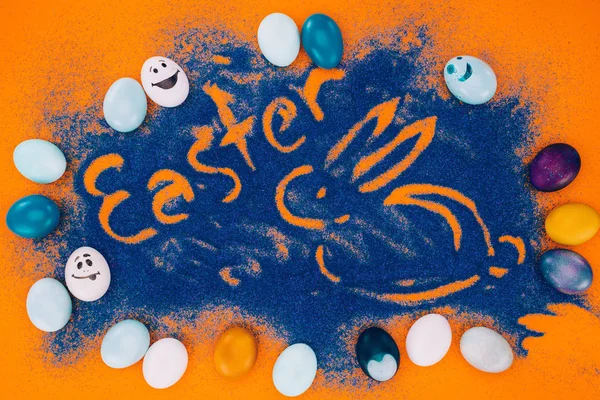 Top view of easter sign with rabbit made of blue sand with chicken eggs on orange — Stock Photo