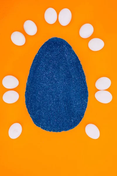 Vista superior de huevo de Pascua azul hecho de arena y huevos de pollo aislados en naranja - foto de stock