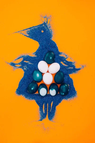 Vista dall'alto del pollo pasquale blu fatto di sabbia con uova dipinte isolate su arancione — Foto stock