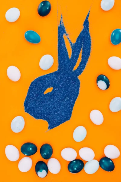 Top view of bunny made of blue sand and easter eggs isolated on orange — Stock Photo