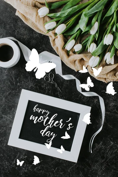 Top view of white tulips, ribbon and mothers day greeting in frame on black surface — Stock Photo