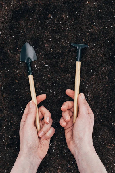Обрезанный снимок человеческих рук с небольшими садовыми инструментами над почвой — стоковое фото