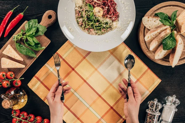 Immagine ritagliata di donna che tiene forchetta e cucchiaio vicino al piatto con la pasta — Foto stock