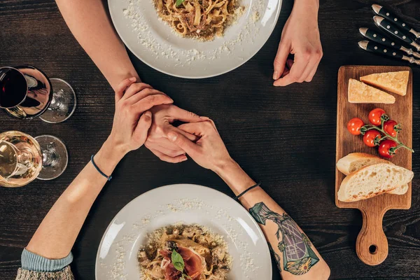 Imagen recortada de pareja lesbiana cogida de la mano en la mesa con comida - foto de stock