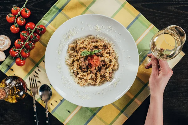 Cropped image of woman holding glass of wine near plate with pasta — Stock Photo