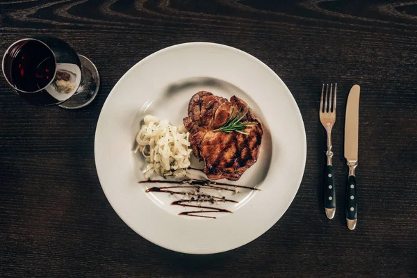 Vue du dessus de l'assiette avec steak de boeuf et verre de vin rouge sur la table — Photo de stock