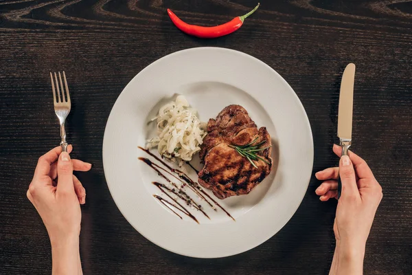 Cropped image of woman holding fork and knife near plate with beef steak — Stock Photo