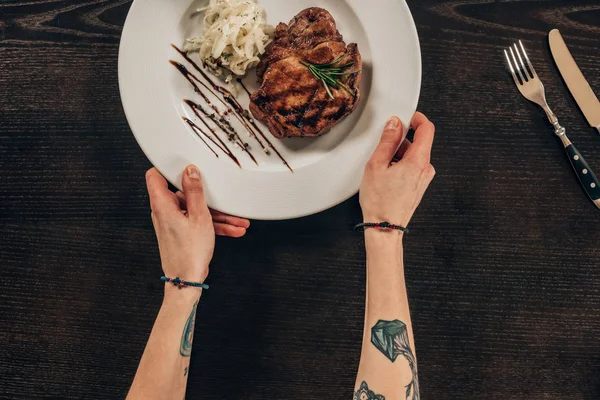 Imagen recortada de la mujer poniendo plato con carne de res en la mesa - foto de stock