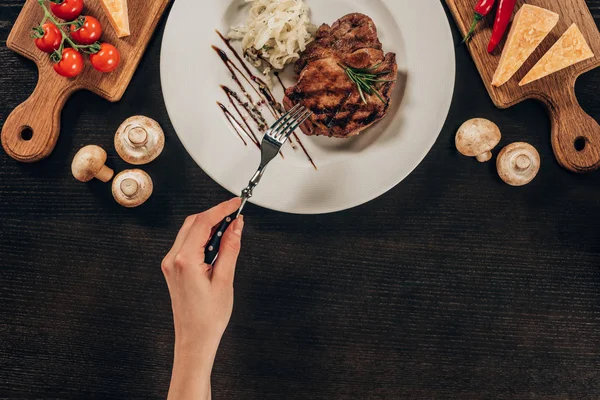 Cropped image of woman holding fork and going to eat beef steak — Stock Photo