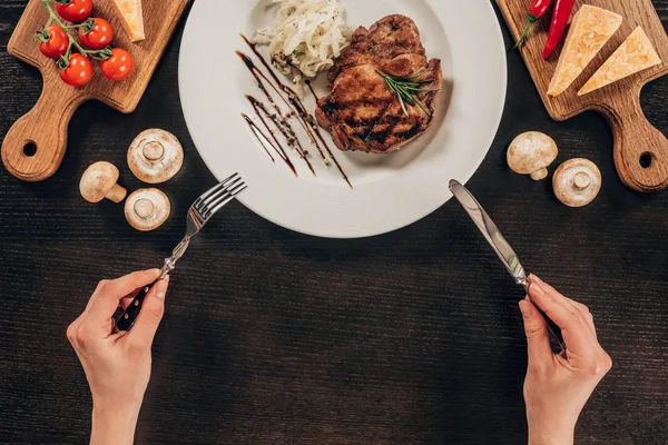 Imagen recortada de la mujer sosteniendo tenedor y cuchillo sobre el plato con filete de carne de res - foto de stock