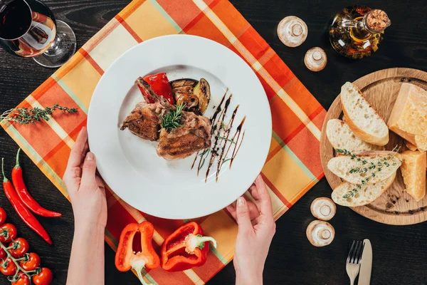 Imagen recortada de mujer poniendo plato con pollo a la parrilla en la mesa - foto de stock