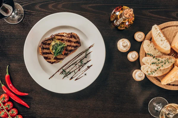 Draufsicht auf Rindersteak auf Teller, Pilze und Baguette auf Tisch — Stockfoto