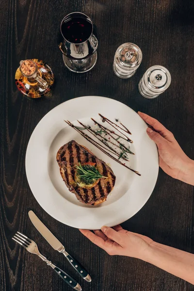 Imagem cortada de mulher colocando prato com bife de carne na mesa — Fotografia de Stock