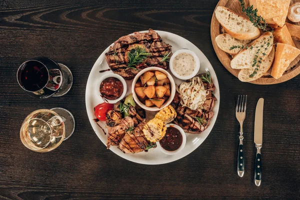 Vista superior de prato com bifes de carne, asas de frango e vinho com queijo na mesa de madeira — Fotografia de Stock