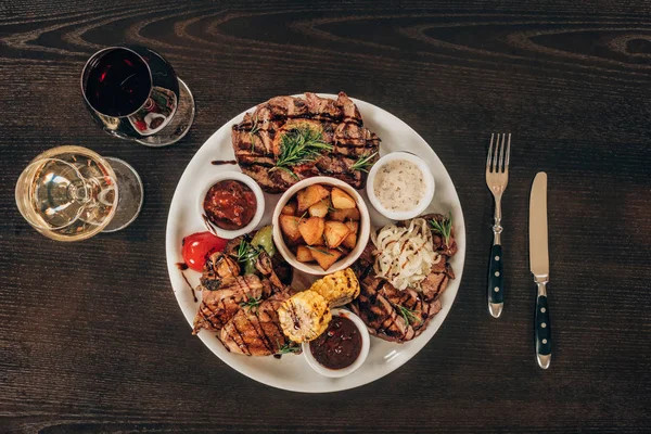 Top view of plate with beef steaks, chicken wings and wine on wooden table — Stock Photo