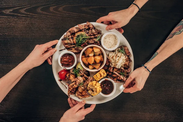 Cropped image of lesbian couple holding plate with beef steaks, chicken wings and grilled vegetables — Stock Photo