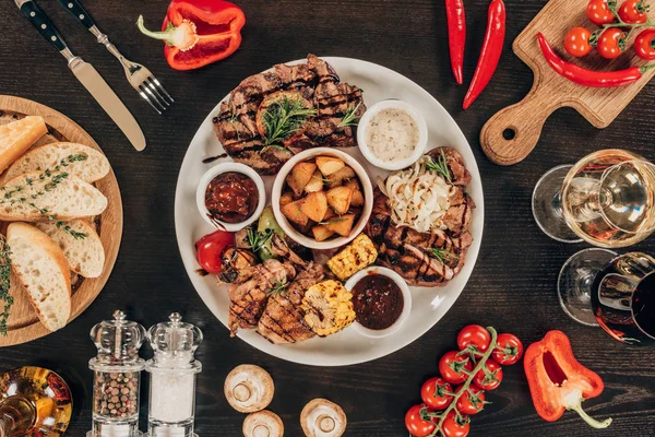 Вид сверху на тарелку со стейками из говядины, овощами и вином на столе — стоковое фото