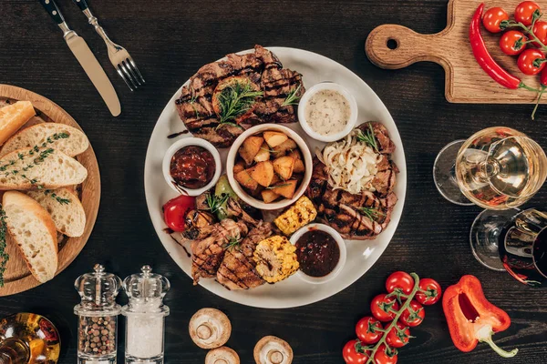 Vista superior da placa com bifes de carne, asas de frango e legumes grelhados na mesa — Fotografia de Stock