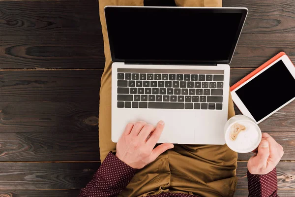 Вид сверху сидящего человека с чашкой кофе, ноутбуком и цифровой табличкой — стоковое фото