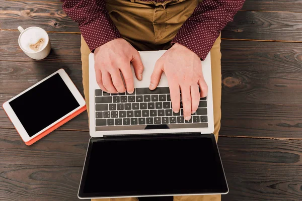 Вид сверху на бизнесмена, сидящего за цифровым столом, чашкой кофе и ноутбуком с экраном для Blank — стоковое фото