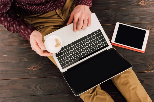 Вид сверху бизнесмена, сидящего с чашкой кофе, цифровым планшетом и ноутбуком с экраном Blank — стоковое фото