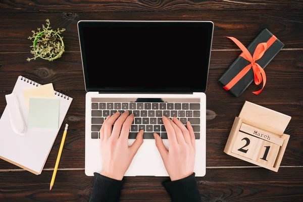 Vista cortada das mãos da mulher no laptop com tela em branco, calendário, caixa de presente, livro didático e planta — Fotografia de Stock