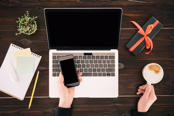 Image recadrée de femme d'affaires avec smartphone, tasse à café, ordinateur portable et boîte cadeau — Photo de stock