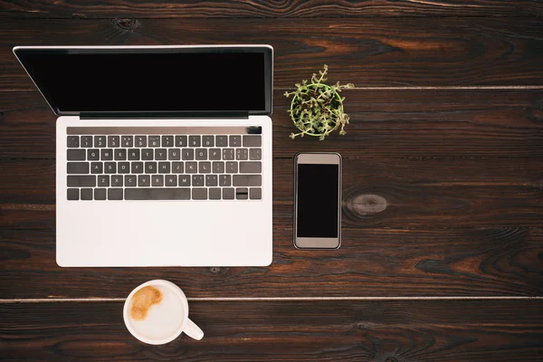 Vue du dessus de l'ordinateur portable avec écran vierge, tasse à café, smartphone et plante en pot — Photo de stock