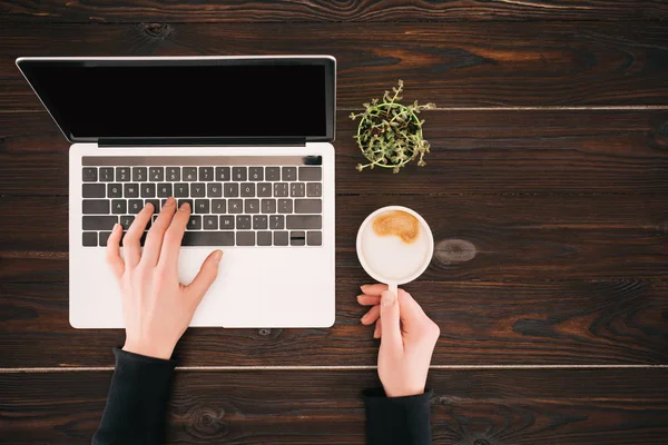 Vista recortada de las manos de la mujer en el ordenador portátil con pantalla en blanco y taza de café - foto de stock