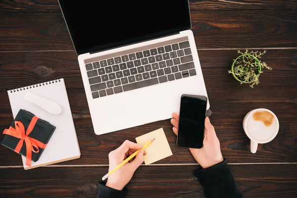 Cropped image of businesswoman hands holding smartphone and pencil, laptop — Stock Photo