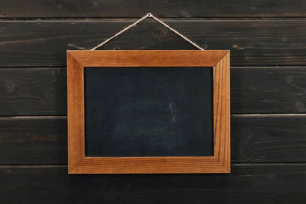 Empty blackboard hanging on wooden wall — Stock Photo