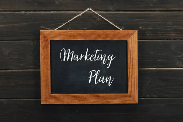 Board with lettering marketing plan hanging on wooden wall — Stock Photo