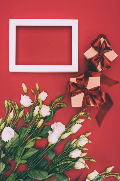 Vista dall'alto di scatole regalo, cornice vuota e bellissimi fiori di eustoma sul rosso — Foto stock