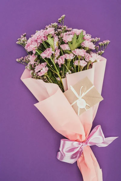 Bouquet of beautiful pink flowers and decorative envelope on violet — Stock Photo