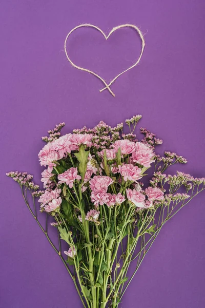 Bouquet of beautiful pink flowers and heart-shaped rope on violet — Stock Photo