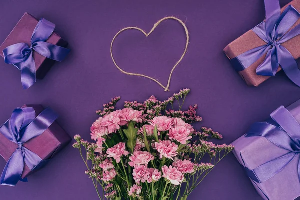 Bouquet of beautiful pink flowers, heart-shaped rope and gift boxes on violet — Stock Photo