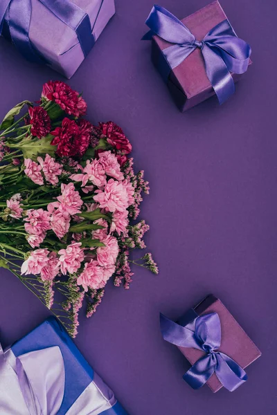 Красивые цветущие цветы и подарки с лентами на фиолетовой — стоковое фото