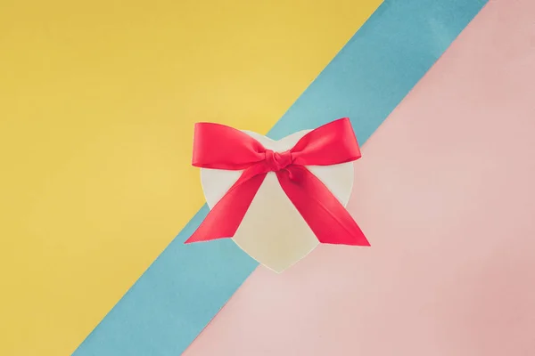 Vista superior de regalo en forma de corazón blanco con cinta rosa sobre fondo colorido - foto de stock