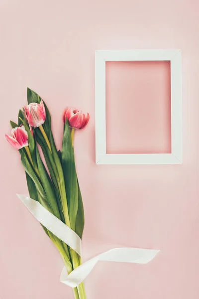 Bouquet di bellissimi tulipani rosa con nastro e cornice bianca vuota su rosa — Foto stock