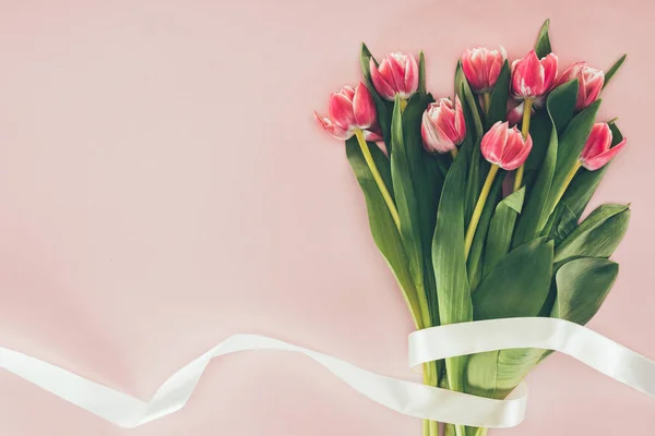 Strauß schöner rosa Tulpen mit grünen Blättern und Band auf rosa — Stockfoto