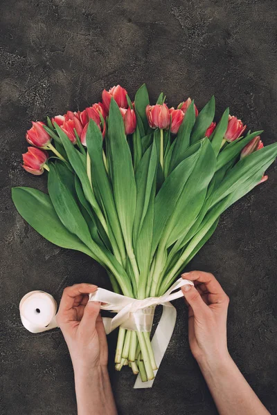 Partial view of person decorating bouquet of beautiful tulips with ribbon — Stock Photo