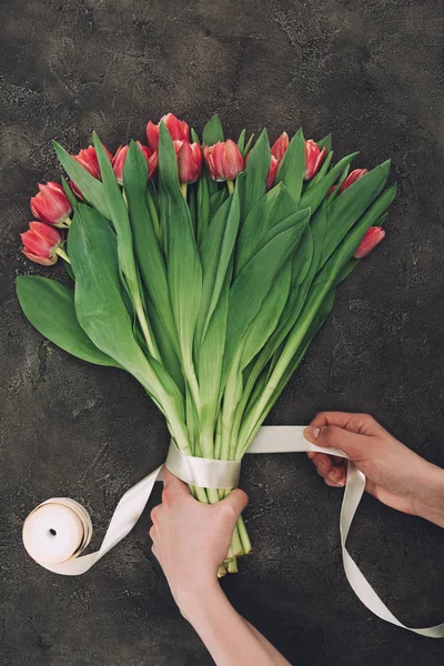 Tiro recortado de persona decorando ramo de hermosos tulipanes con cinta - foto de stock