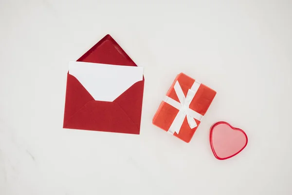 Composição vista superior do envelope vermelho com papel em branco e caixas de presente isoladas em branco — Fotografia de Stock