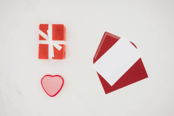 Vue du dessus de l'enveloppe rouge ouverte avec du papier vierge et des boîtes-cadeaux isolées sur blanc — Photo de stock