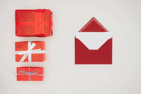 Vue du dessus de l'enveloppe rouge avec papier blanc et rangée de boîtes-cadeaux isolées sur blanc — Photo de stock