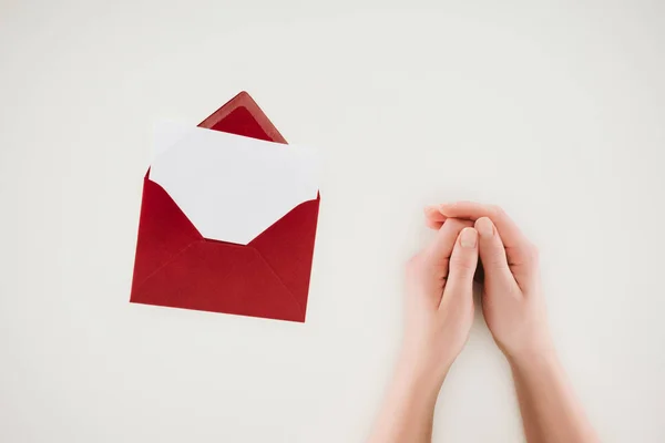 Обрезанный снимок женщины, держащейся за руки рядом с открытым красным конвертом с чистой бумагой, изолированной на белом — стоковое фото